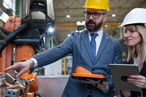 Chief engineer and project manager in modern industrial factory with robot arms talking and planning optimization of production.