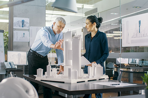 Chief Male Architect and Female Engineer Work with City Buildings Model. Bright People Work as Urban Planners.