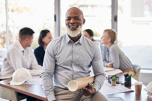 Black man, architect and portrait smile with blueprint in team planning for construction or building at office. African senior leader CEO contractor or engineer with floor plan in architecture